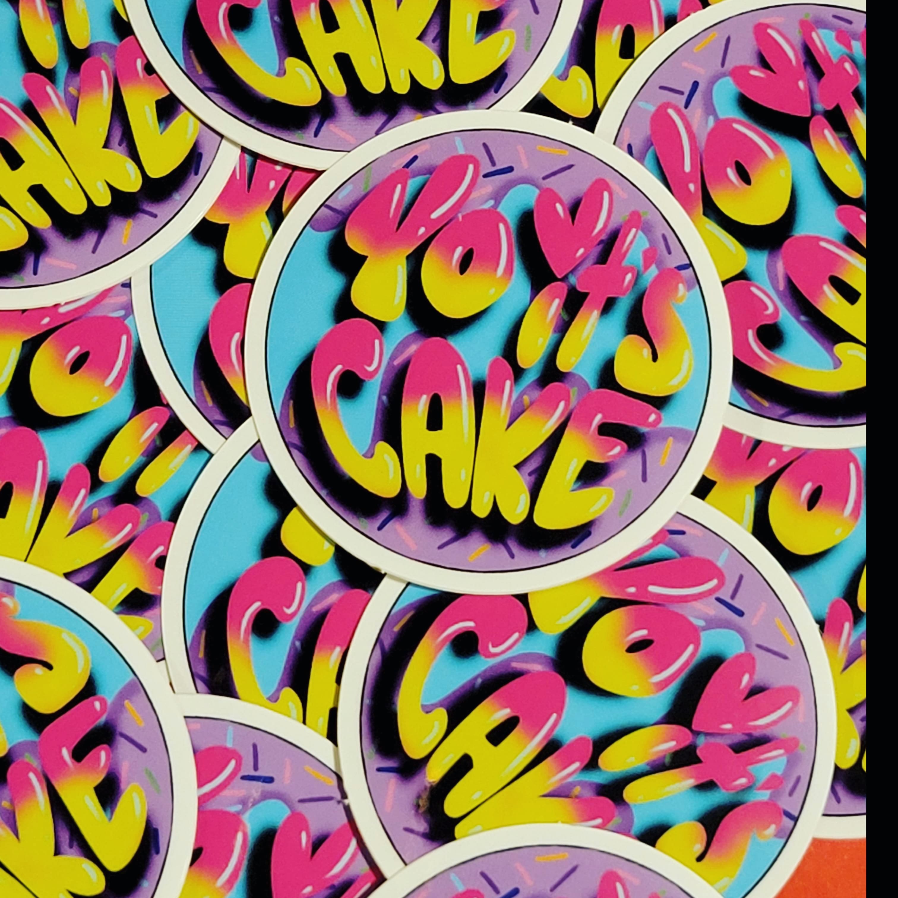 Photo of several "yo its cake" logo stickers in a layered pile.